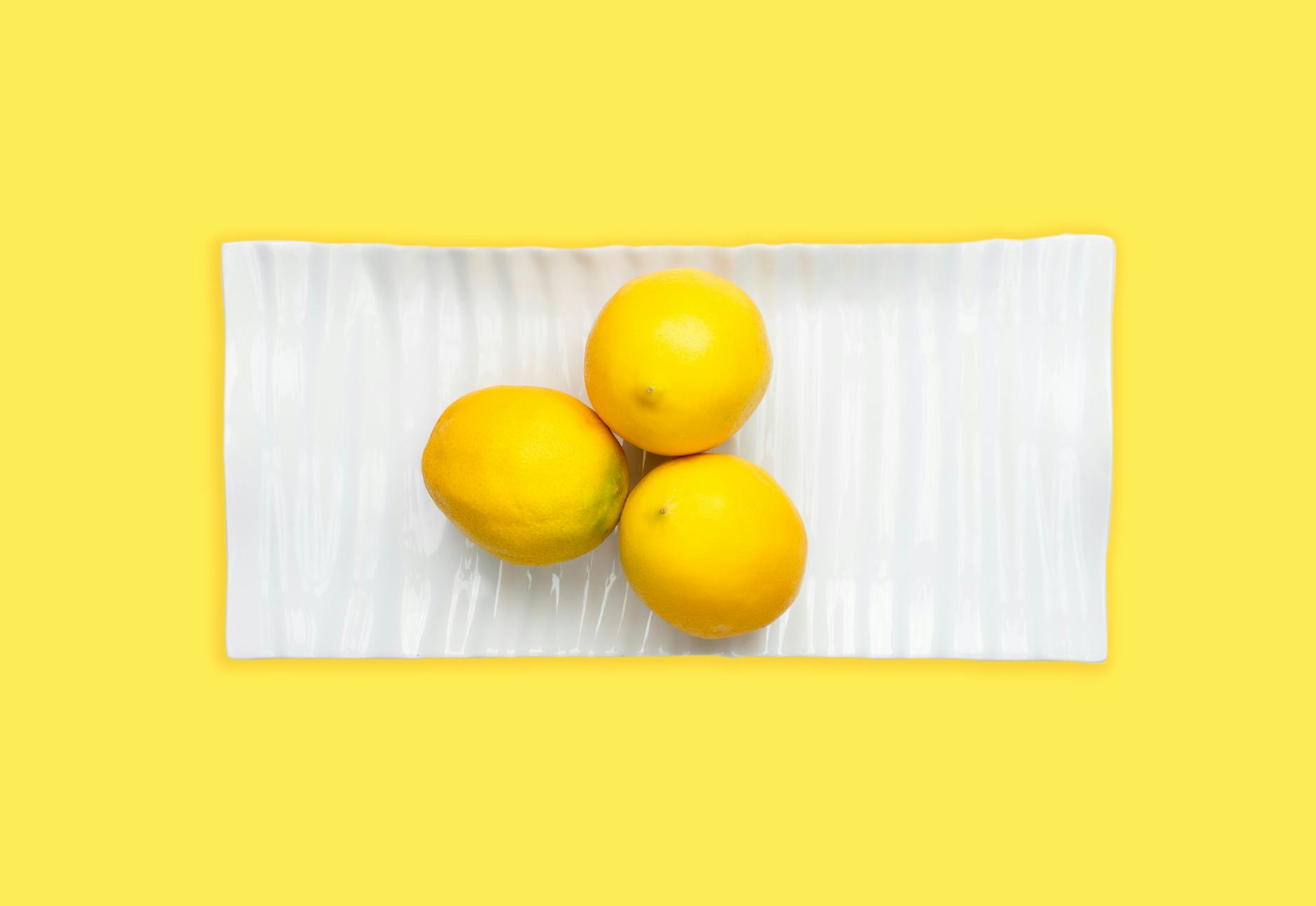 Fresh lemons arranged on a white plate with vibrant yellow background, symbolizing restored sensation and vitality