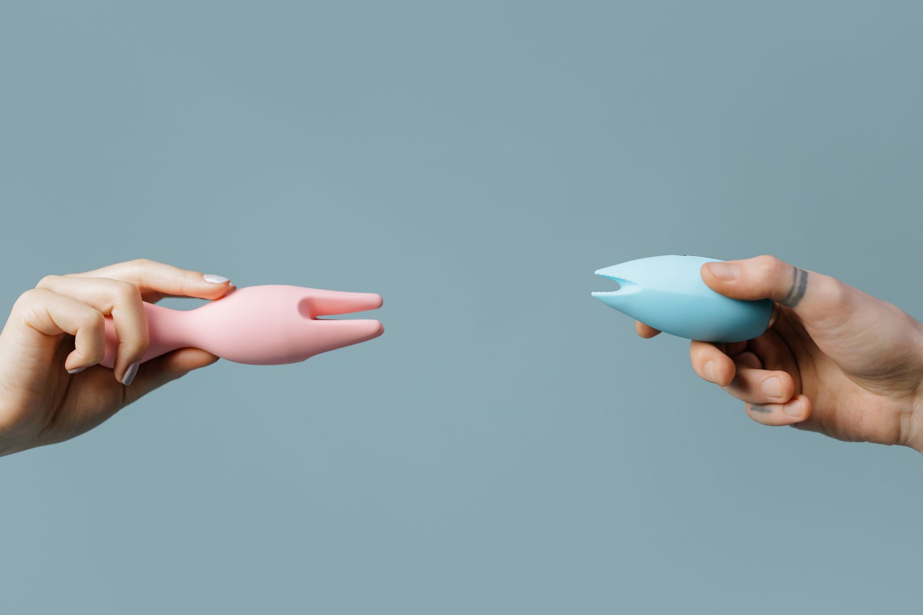 Woman holding blue and pink clitoral vibrators in a thoughtful expression