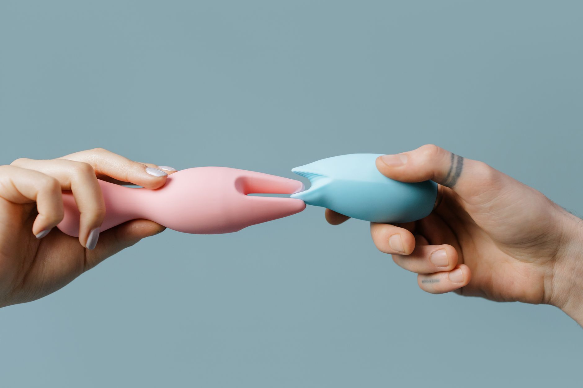 Uma mão segurando um vibrador clitoral colorido entre uma variedade de brinquedos sexuais em uma mesa