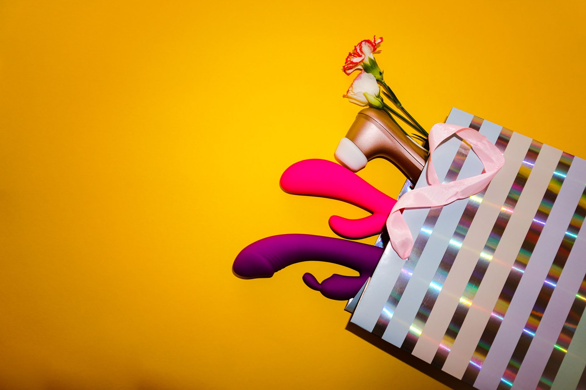 Colorful lemon vibrators and intimate wellness products in a holographic gift bag against a bold yellow background